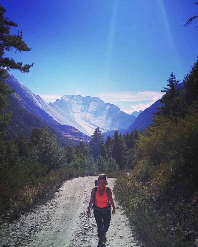Melanie Bauer mit Rucksack auf einem Bergweg, dahinter Wald und Berge